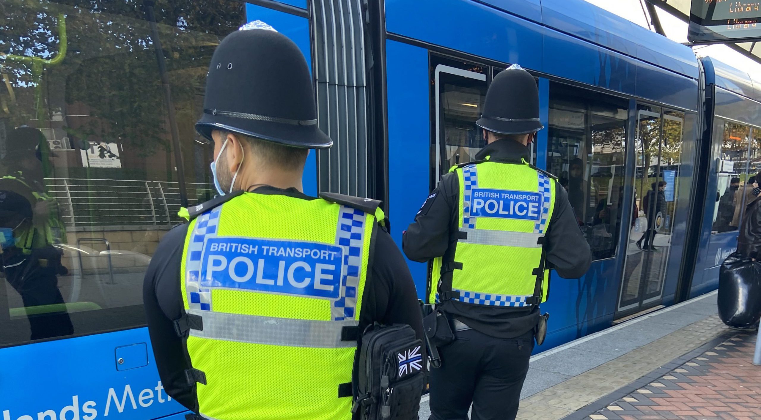Two British transport police officers walking along tram platform looking at trams