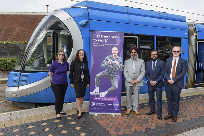 Two women and three men standing in front of tram next to roller banner sign promoting West Midlands Metro